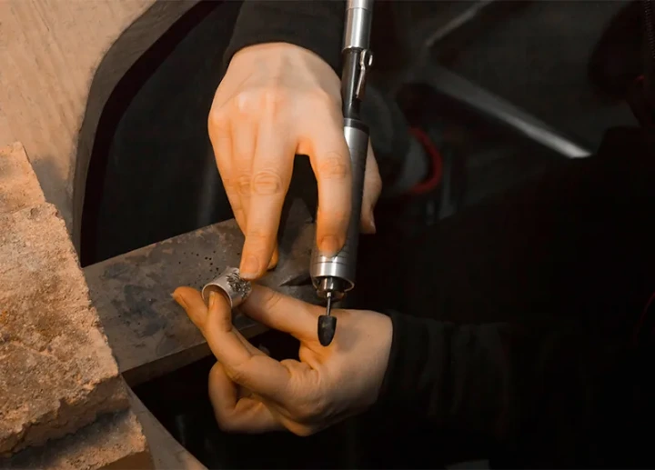 Une femme qui travaille une bague artisanale en métal à la ponceuse